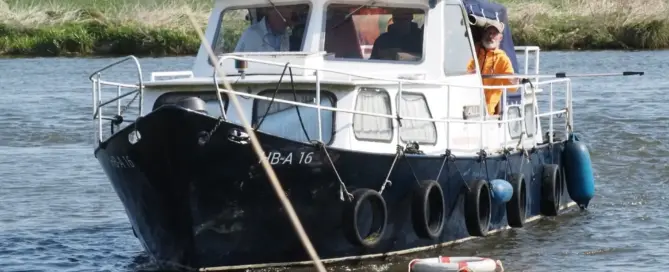 Schwarz-weißes Motorboot mit Passagieren auf einem Fluss, umgeben von Pflanzen.