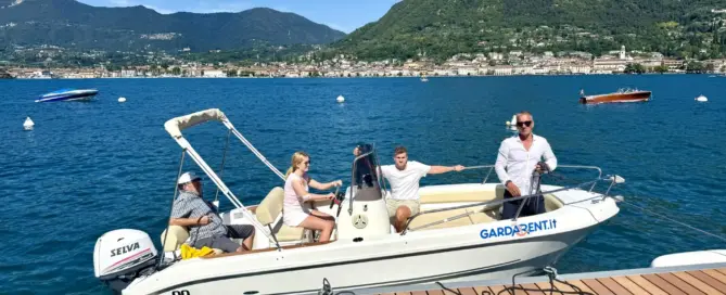 Ein Motorboot mit vier Personen fährt auf einem klaren Wasser vor einer Berglandschaft.