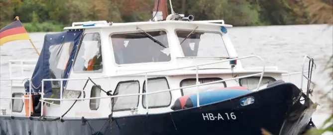 Schwarzes Motorboot mit der Kennung HB-A 16 auf einem Fluss, umgeben von Bäumen und Pflanzen.