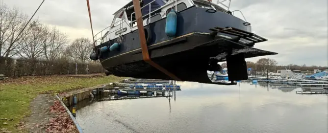 Ein Boot wird mit einem Kran über das Wasser gehoben, während es an einem Hafen befestigt ist.