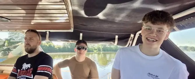 Drei frisch geprüfte Teilnehmer sitzen lachend an Bord eines Motorbootes auf der Weser bei Sonnenschein nach dem Sportbootführerschein See und Binnen.
