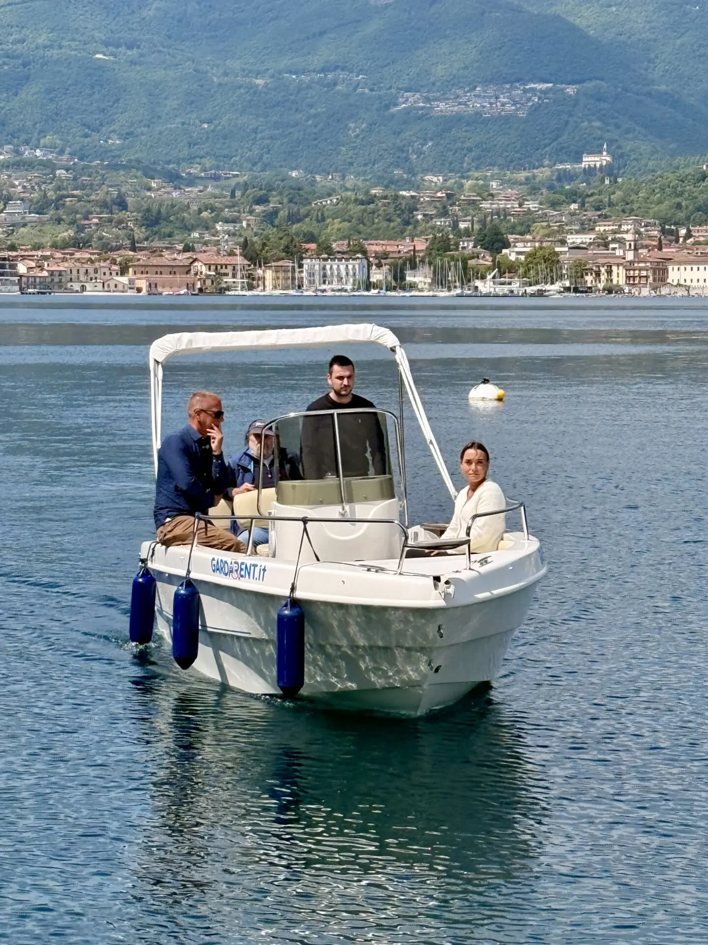 ab-sportbootschule_pruefung_30-04-2026_05 Bei strahlendem Sonnenschein fährt eine Prüfungsgruppe mit dem Motorboot auf dem Gardasee, während Lazise und die Berge im Hintergrund liegen.