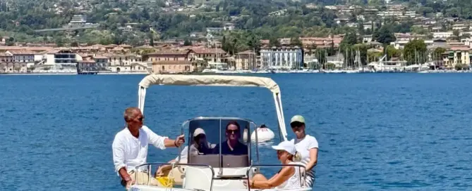 Vor San Felice del Benaco fährt ein kleines Motorboot mit mehreren Personen über den blauen See.
