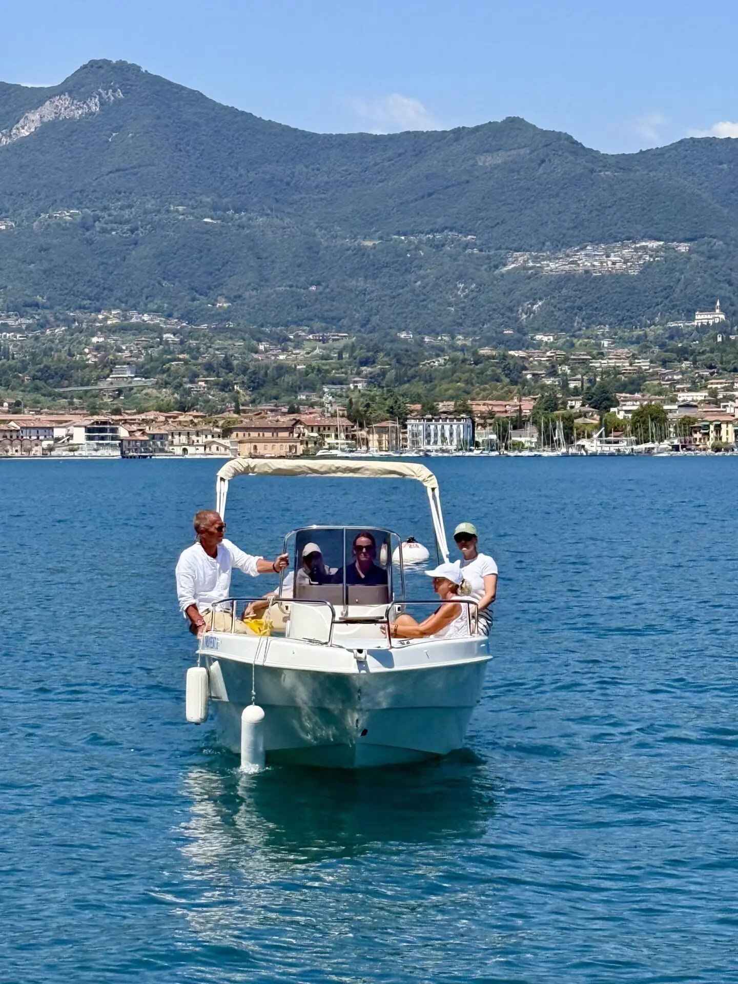 Vor San Felice del Benaco fährt ein kleines Motorboot mit mehreren Personen über den blauen See.