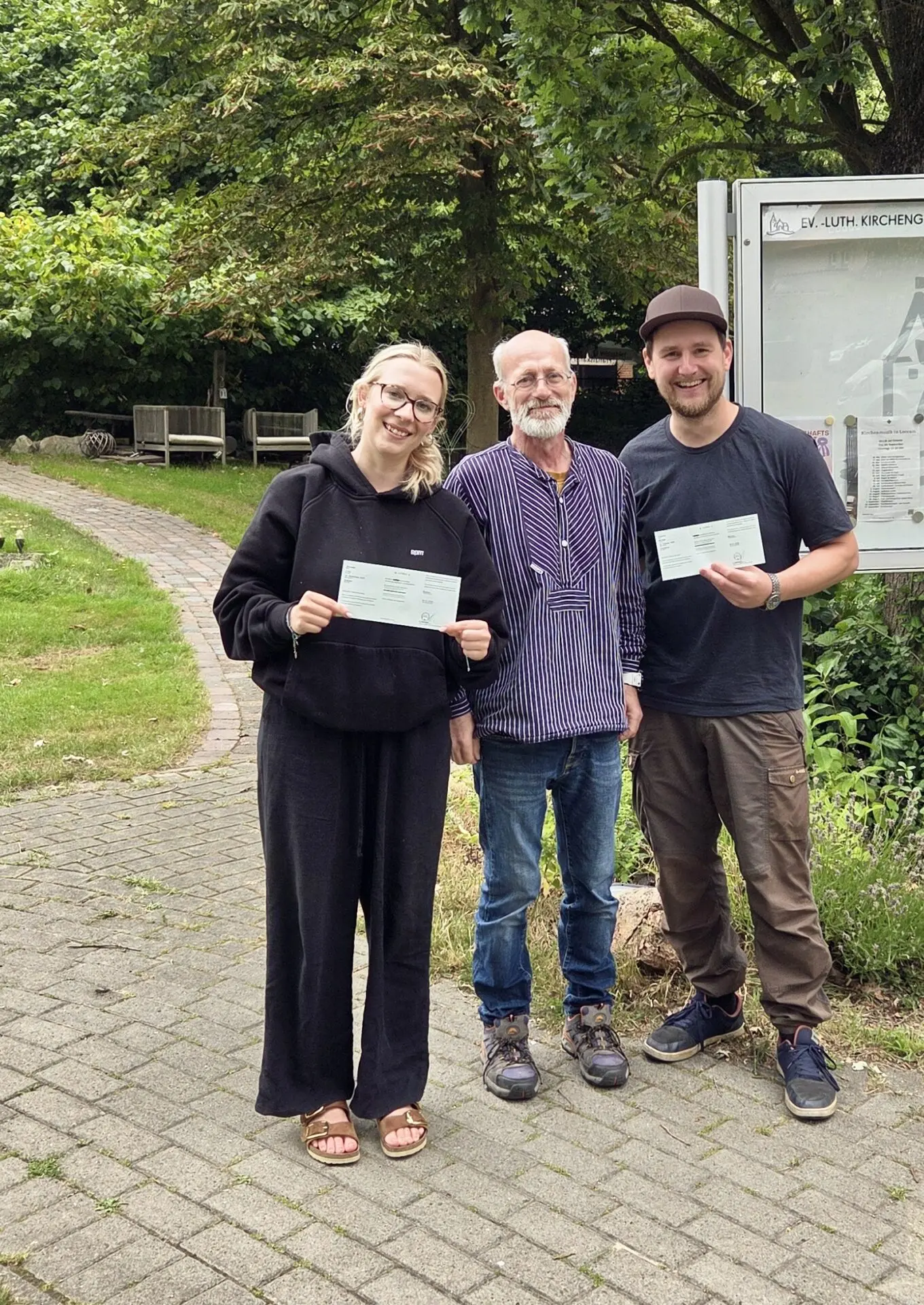 Zwei frischgebackene Prüflinge und ein Mann stehen vor Bäumen und halten ihre Prüfungsurkunden an der Weser.