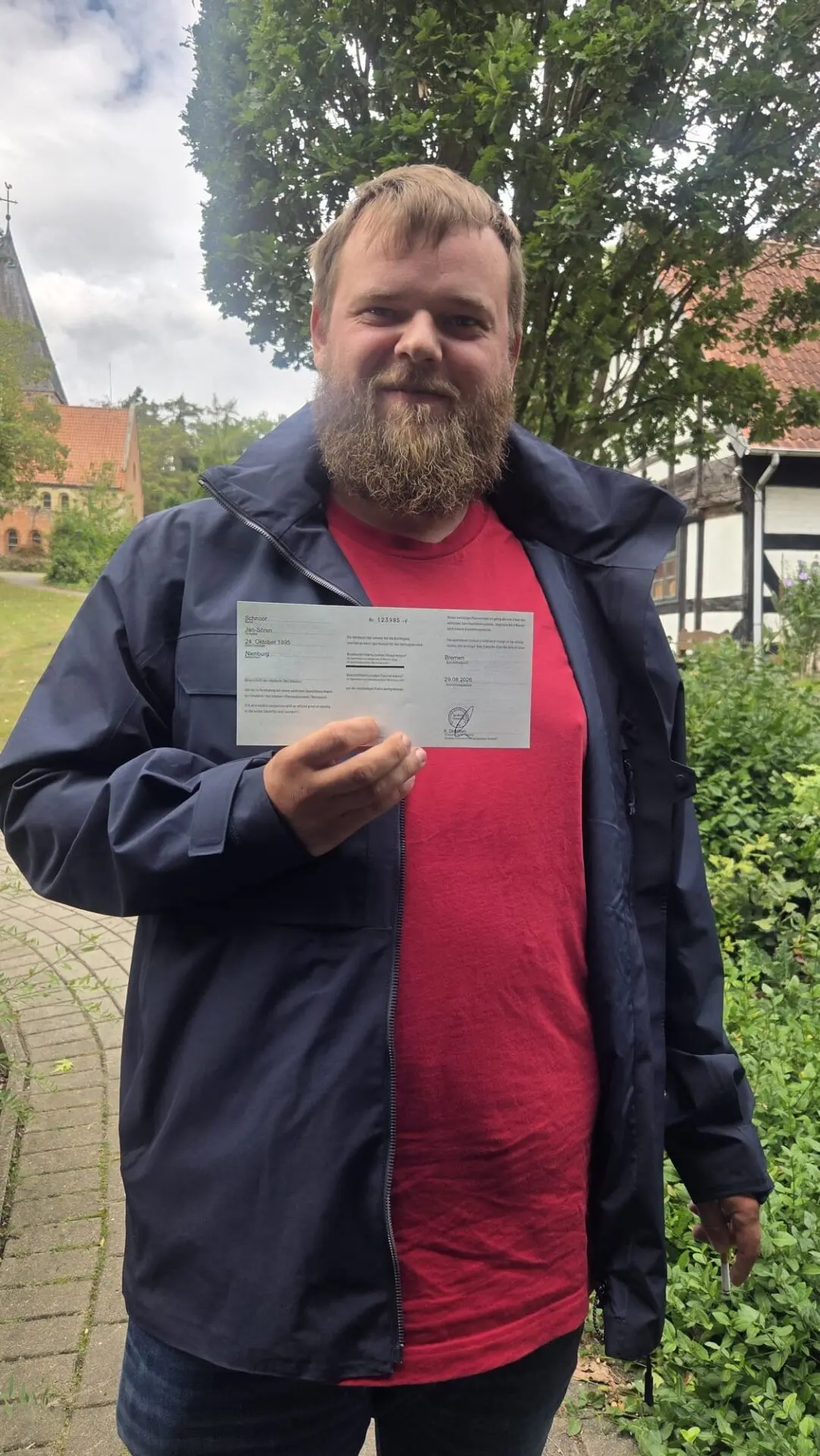 Ein Teilnehmer hält nach bestandener Sportbootführerschein-Prüfung seine Bescheinigung vor einem Gebäude an der Weser.